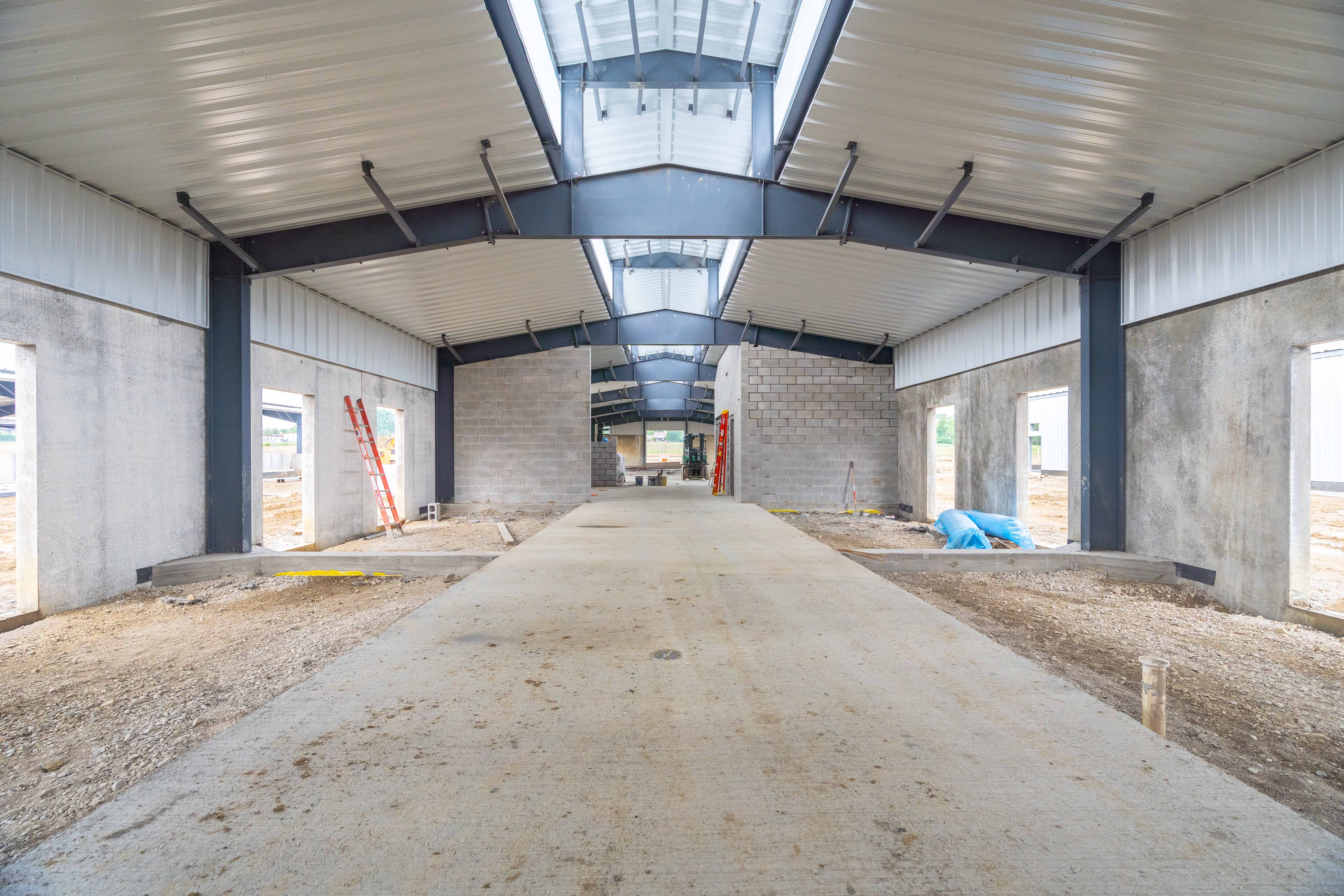 A view inside a barn where concrete is seen down the middle and dirt floors along the sides for horse stalls.