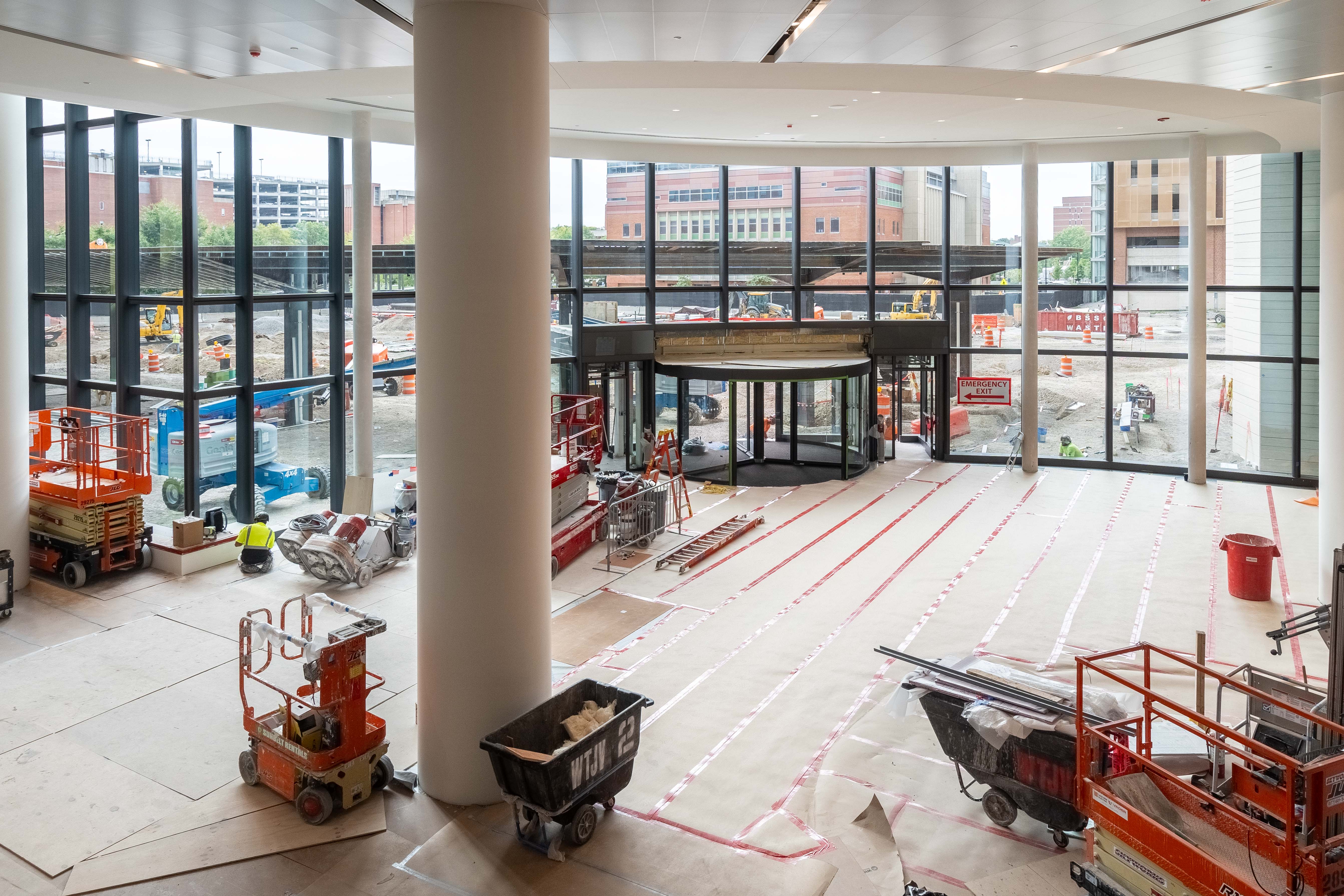 A view of the ground floor lobby from the second floor. A large revolving door is seen with construction equipment all around the room. 