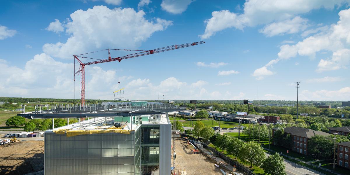 A wide view of the crane and building as a crane carries a solar panel. 