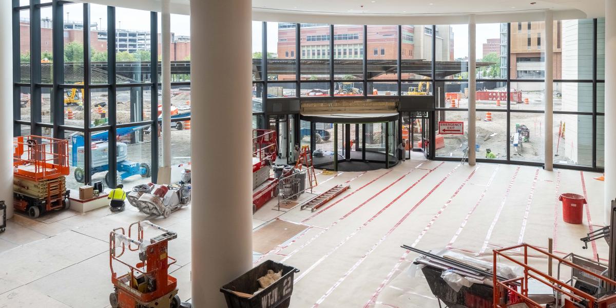 A view of the ground floor lobby from the second floor. A large revolving door is seen with construction equipment all around the room. 